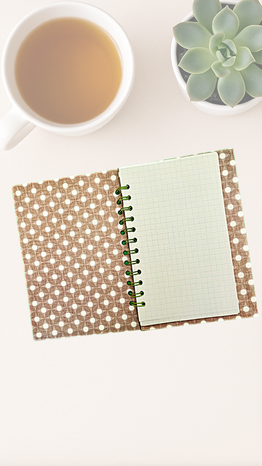 Open spiral notebook with a patterned inside cover next to a cup of tea and a succulent plant on a white surface