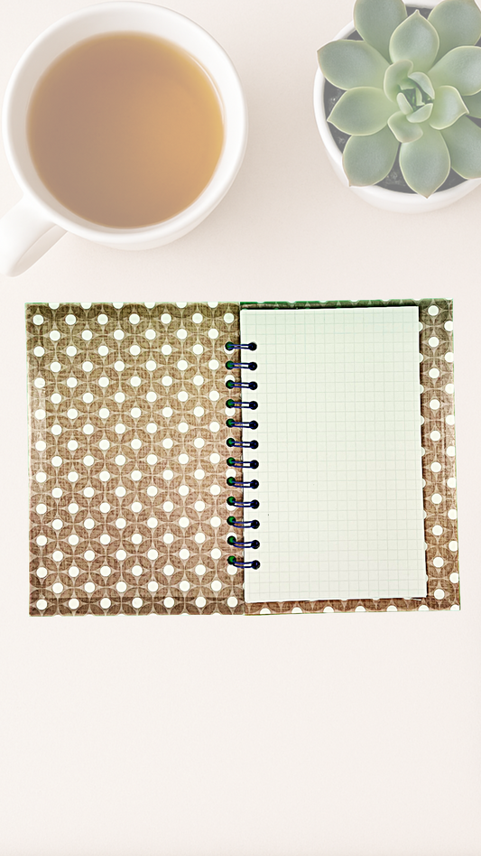 Open notebook with geometric inside cover design next to a cup of tea and succulent plant on a white surface