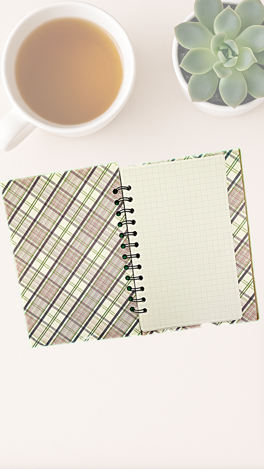 Open notebook with plaid inside cover and green lined pages on a white surface with a cup of tea and succulent plant.