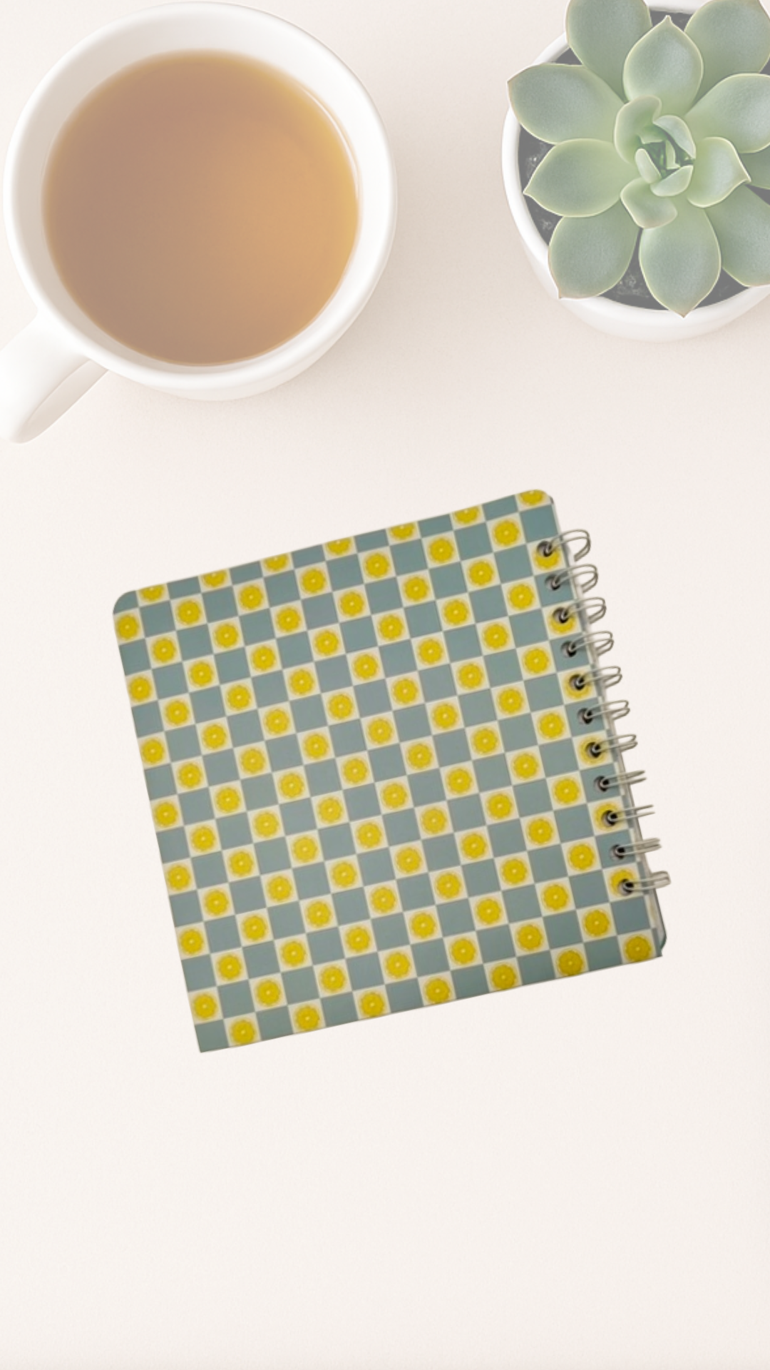 Notebook with a checkered back cover next to a cup of tea and a small plant on a white surface