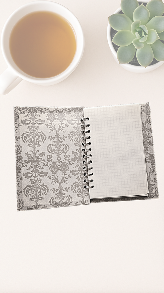 Open notebook with decorative cover on a white surface next to a cup of tea and a succulent plant.