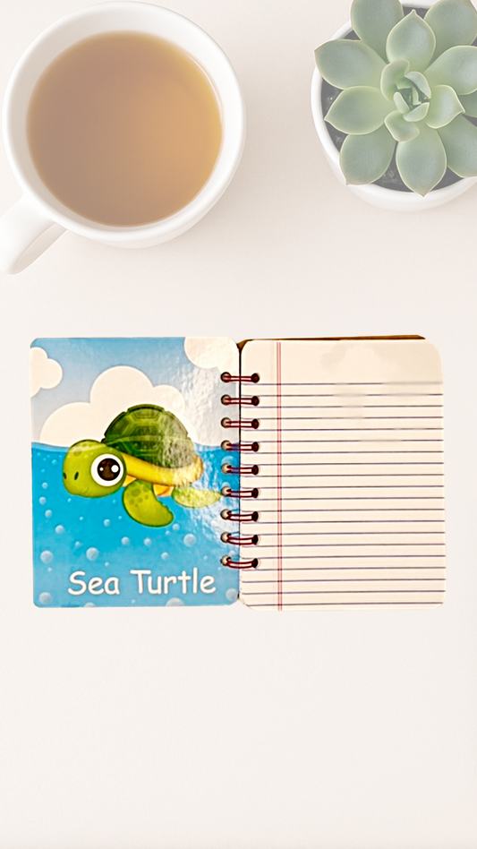 Open spiral notebook with an illustrated sea turtle design on the inside cover, next to a cup of tea and a succulent plant.