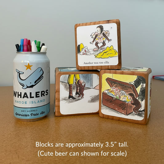 Three wooden blocks with illustrations and a canister with pens on a table.