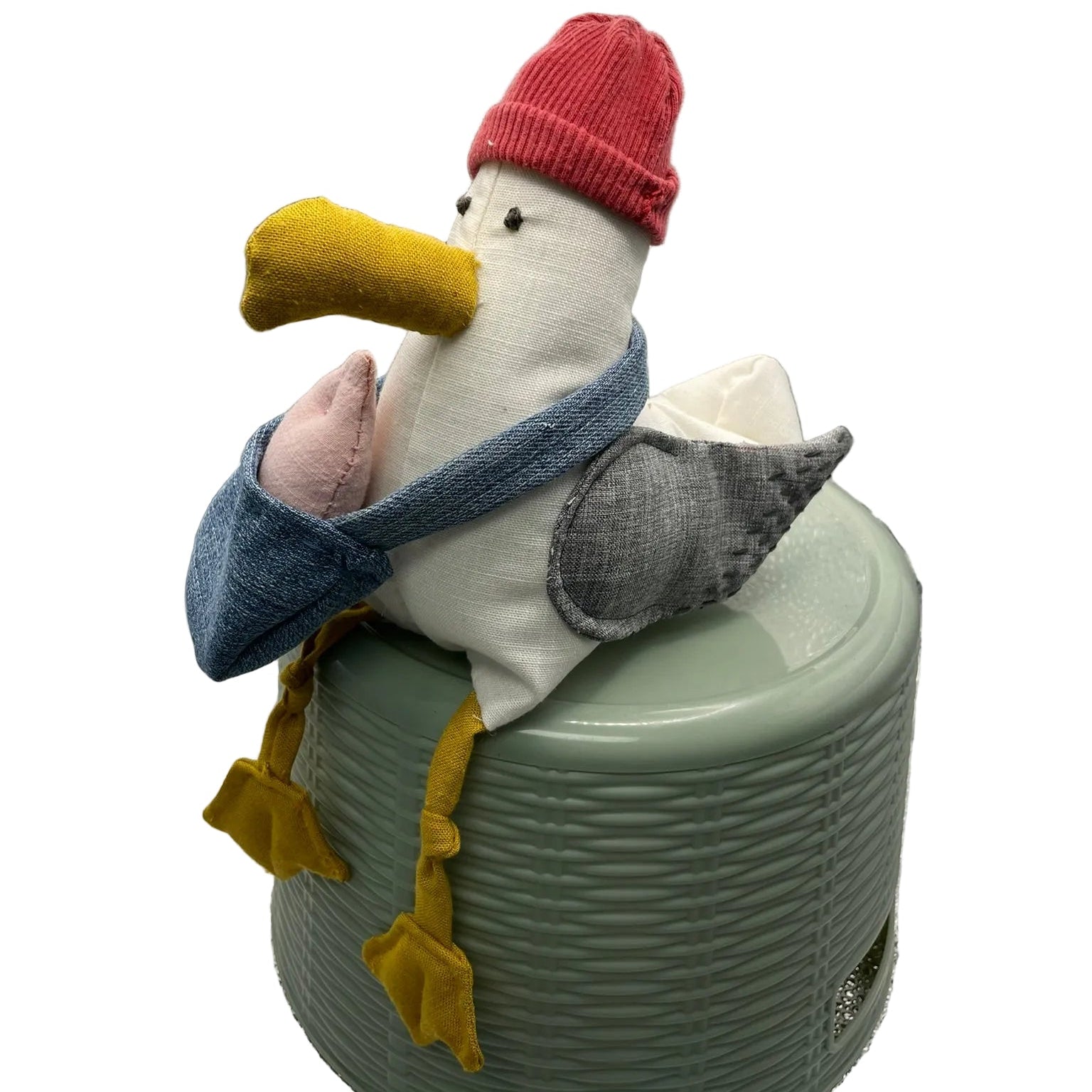 Stuffed toy goose with a red hat and yellow beak on a green container against a textured silver background