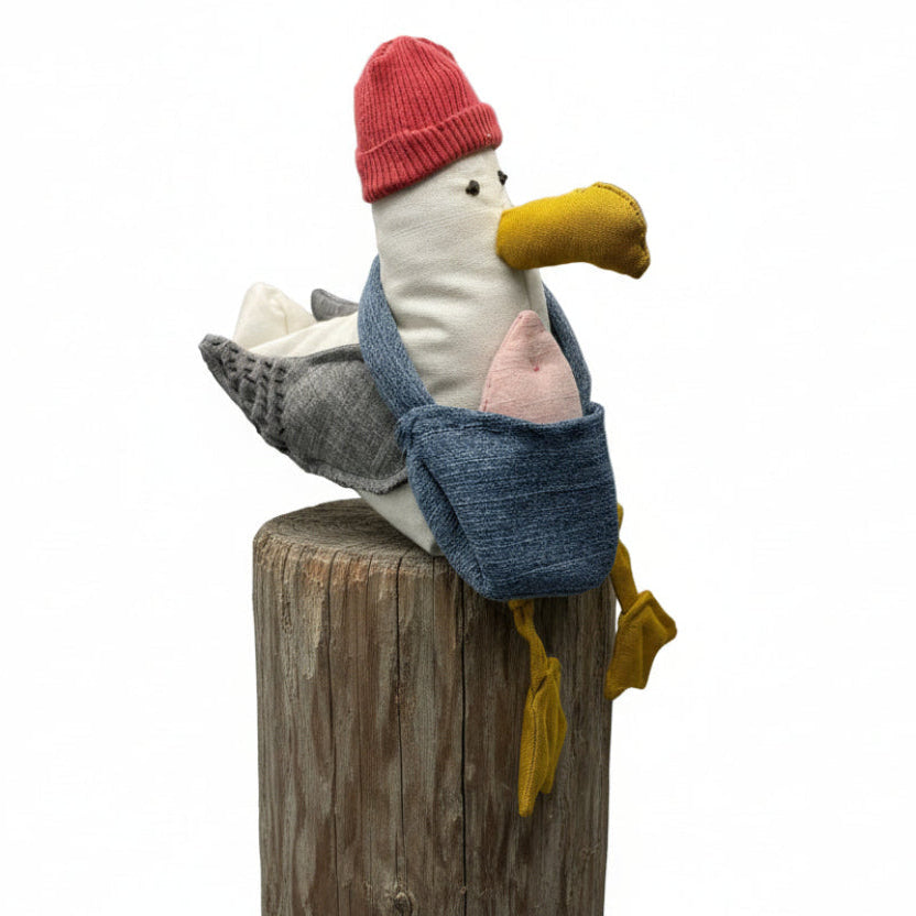 Stuffed toy seagull wearing a red hat and blue bag with pink fish