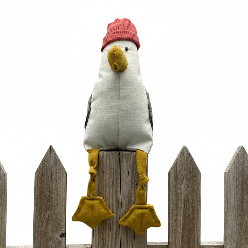 Plush toy seagull wearing a red hat on a textured surface