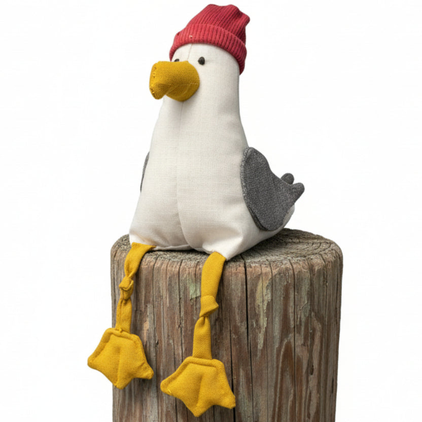 Plush toy seagull with a red hat on a textured surface