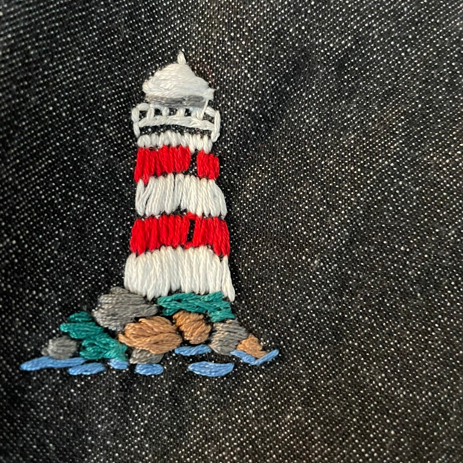 Embroidered lighthouse patch on a dark fabric background