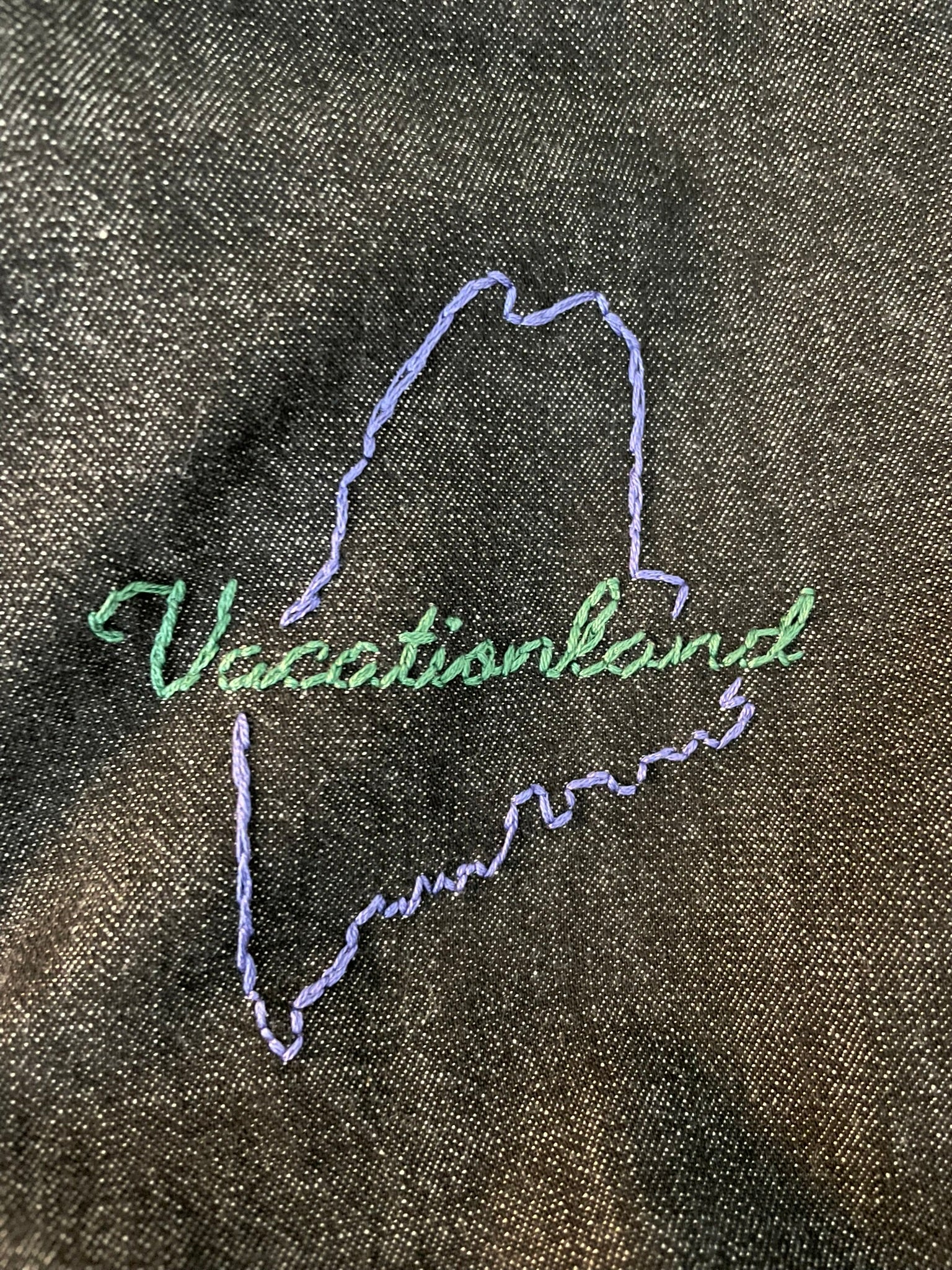 Embroidered design of a state outline with 'Vacationland' on a textured fabric background