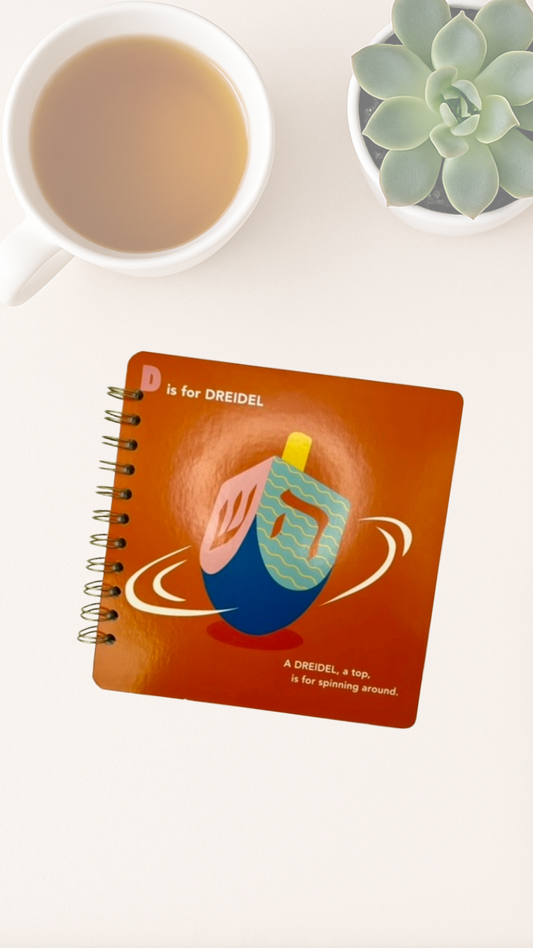 Notebook with a dreidel illustration on a white surface with a cup of tea and succulent plant.