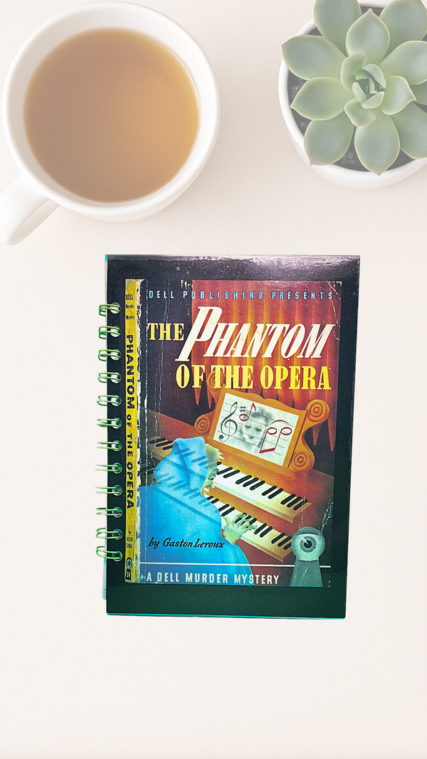 Notebook titled 'The Phantom of the Opera' with a cup of tea and succulent plant on a white surface