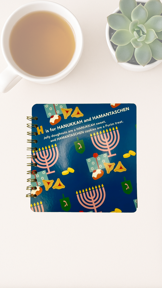 Notebook with Hanukkah-themed cover design next to a cup of tea and succulent plant