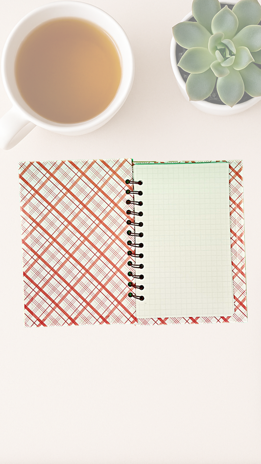 Open notebook with inside covers of plaid and solid designs next to a cup of tea and succulent plant on a white surface