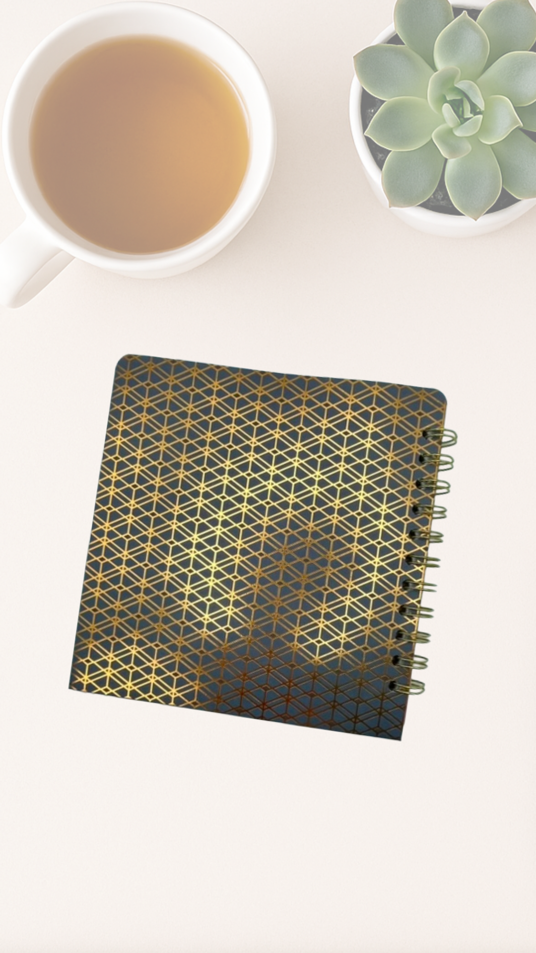 Notebook with geometric back cover on a white surface next to a cup of tea and a succulent plant.