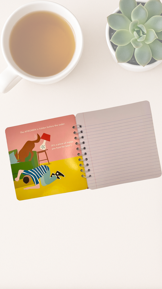 Open spiral-bound notebook with colorful cover on a white surface next to a cup of tea and a small plant.